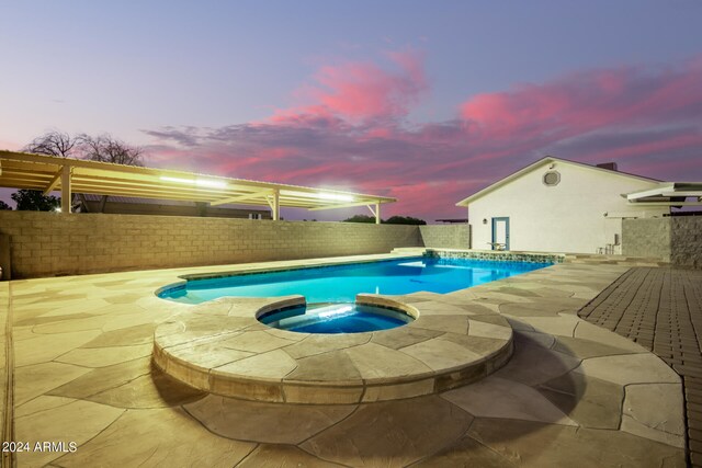 pool at dusk with an in ground hot tub and a patio area