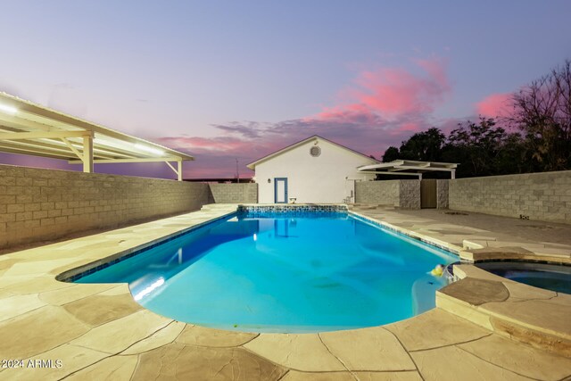 pool at dusk with a patio and an in ground hot tub