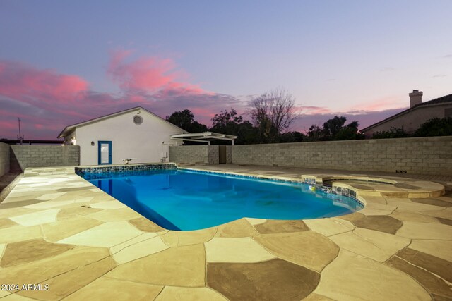 pool at dusk featuring an in ground hot tub and a patio