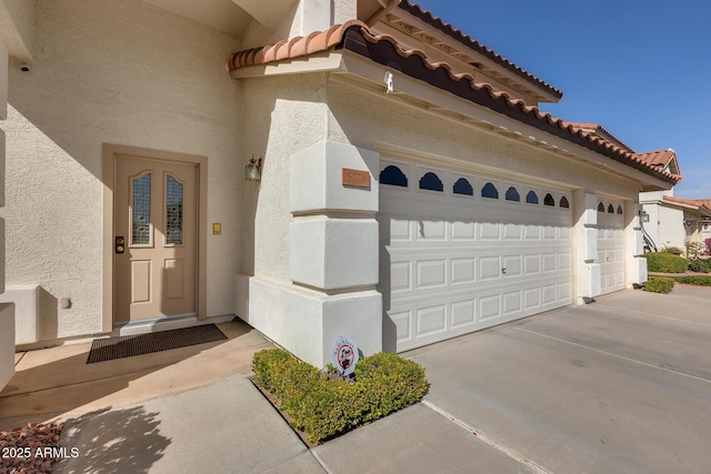 entrance to property with concrete driveway, a tiled roof, and stucco siding