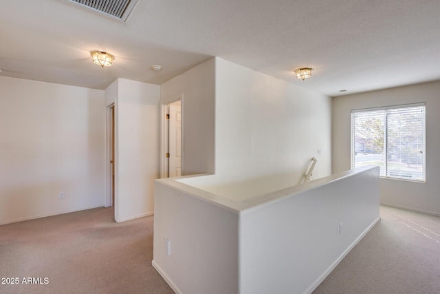 corridor featuring baseboards, a textured ceiling, visible vents, and light colored carpet