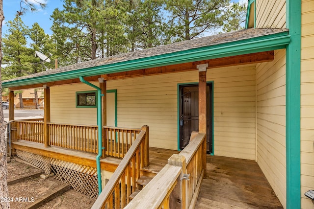 doorway to property featuring a porch and a shingled roof