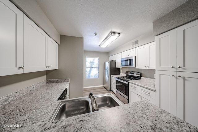 2025 E Campbell Ave Unit 137, Phoenix, AZ 85016 - kitchen with appliances with stainless steel finishes, white cabinets, a textured ceiling, light stone countertops, and light wood-type flooring