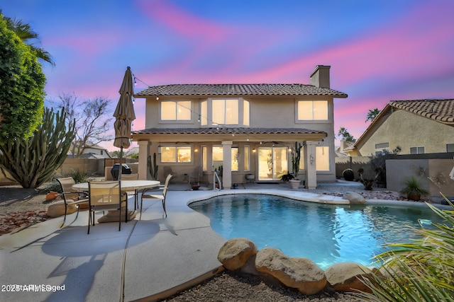 back house at dusk with a fenced in pool and a patio