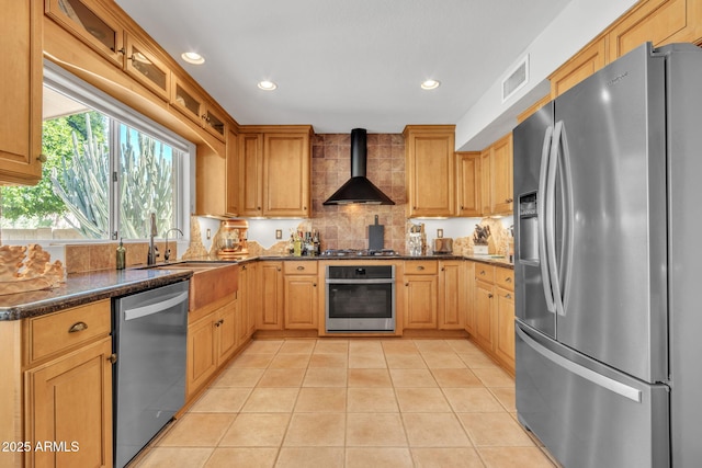 kitchen with light tile patterned flooring, sink, dark stone counters, stainless steel appliances, and wall chimney exhaust hood