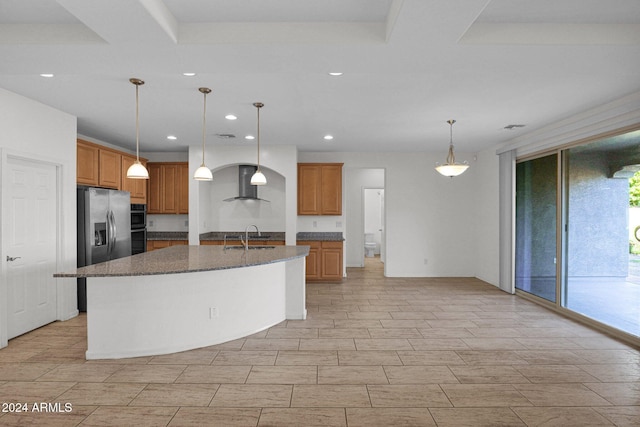 kitchen featuring range hood, stainless steel refrigerator with ice dispenser, decorative light fixtures, and a kitchen island with sink