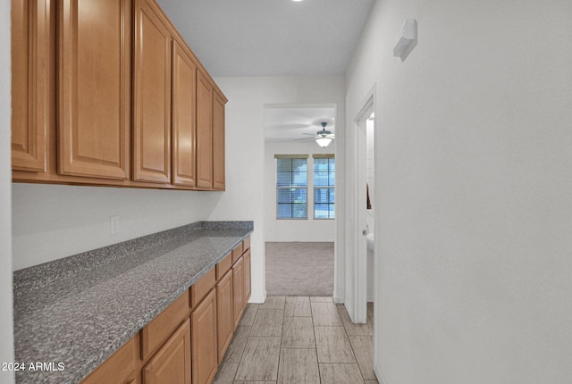 kitchen with dark stone counters, ceiling fan, and light carpet