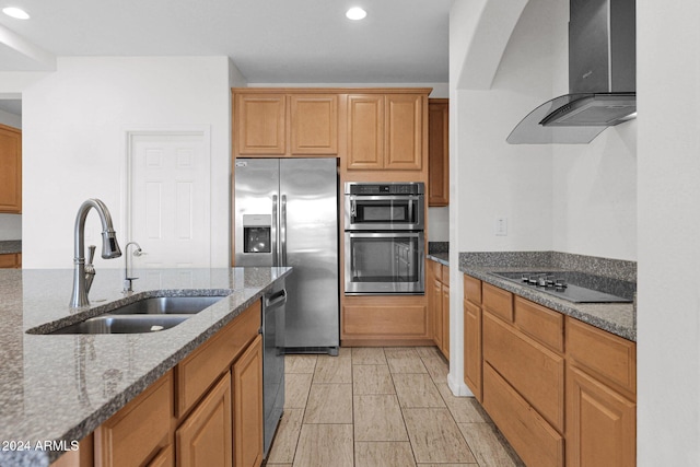 kitchen featuring stone counters, appliances with stainless steel finishes, sink, and wall chimney exhaust hood