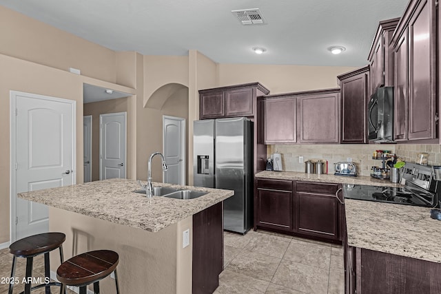 kitchen featuring lofted ceiling, a center island with sink, sink, appliances with stainless steel finishes, and tasteful backsplash