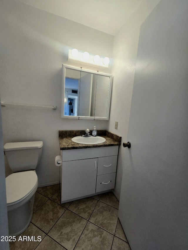 half bath with toilet, vanity, tile patterned floors, and baseboards