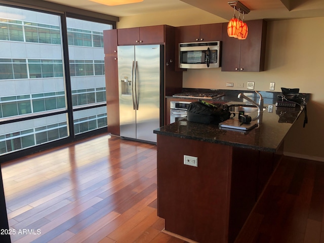 kitchen featuring kitchen peninsula, decorative light fixtures, light wood-type flooring, appliances with stainless steel finishes, and dark stone countertops