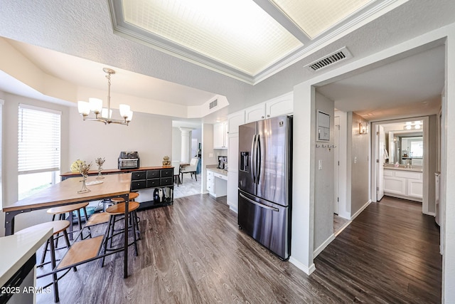 7110 N 28th Dr, Phoenix, AZ 85051 - kitchen featuring stainless steel refrigerator with ice dispenser, white cabinetry, dark wood finished floors, a chandelier, and decorative columns