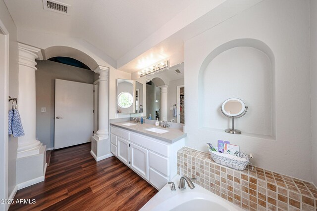 7110 N 28th Dr, Phoenix, AZ 85051 - bathroom featuring decorative columns, wood finished floors, a bath, double vanity, and lofted ceiling