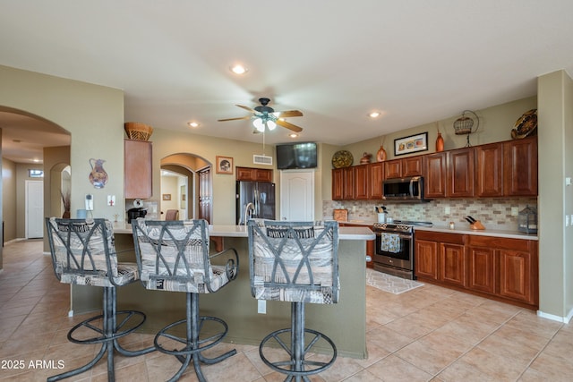 kitchen featuring stainless steel appliances, light tile patterned floors, backsplash, and a kitchen breakfast bar