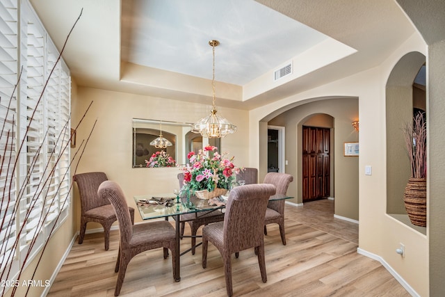 dining space with a tray ceiling, light hardwood / wood-style floors, and a chandelier