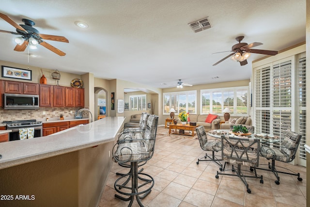 kitchen featuring light tile patterned floors, appliances with stainless steel finishes, a kitchen breakfast bar, a textured ceiling, and decorative backsplash