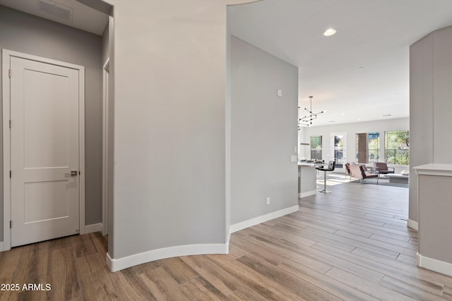 corridor with light hardwood / wood-style flooring and a chandelier