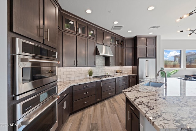 kitchen with light stone counters, appliances with stainless steel finishes, dark brown cabinetry, and sink