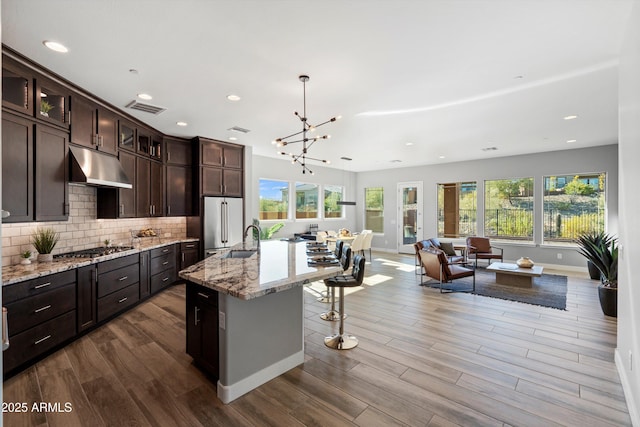 kitchen featuring light stone countertops, a healthy amount of sunlight, decorative light fixtures, a kitchen island with sink, and appliances with stainless steel finishes