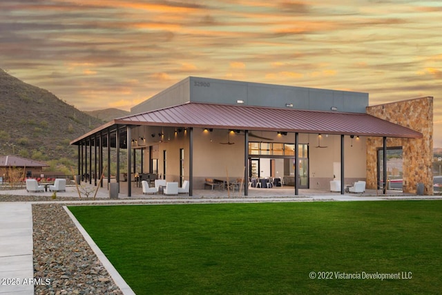 back house at dusk featuring a lawn, a patio area, ceiling fan, and a mountain view