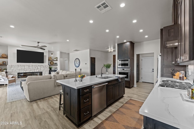 kitchen with a fireplace, appliances with stainless steel finishes, sink, an island with sink, and a breakfast bar