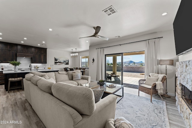 living room with a fireplace, ceiling fan with notable chandelier, and light hardwood / wood-style flooring