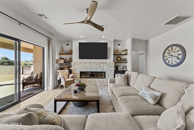 living room with a stone fireplace, light hardwood / wood-style floors, and ceiling fan