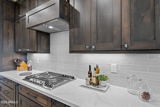 kitchen featuring dark brown cabinets, stainless steel gas stovetop, backsplash, and light stone counters