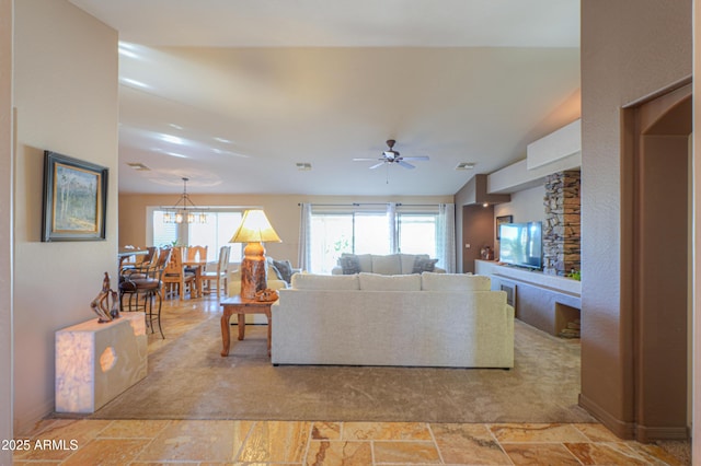 living room with lofted ceiling, a wealth of natural light, and ceiling fan with notable chandelier