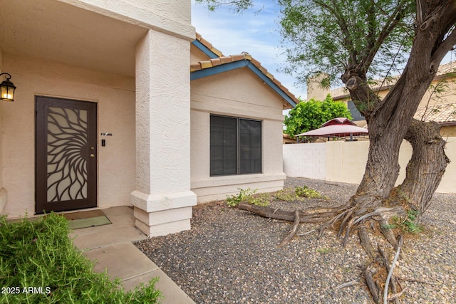 entrance to property featuring a tiled roof, fence, and stucco siding