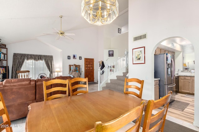 dining room with visible vents, arched walkways, stairs, high vaulted ceiling, and ceiling fan with notable chandelier