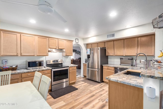 kitchen featuring light stone counters, stainless steel appliances, visible vents, a sink, and under cabinet range hood