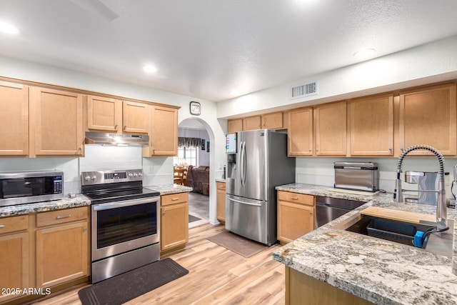 kitchen with arched walkways, under cabinet range hood, stainless steel appliances, a sink, and visible vents