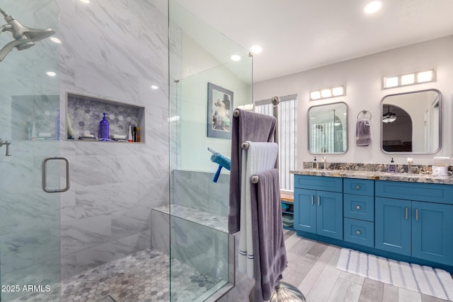 bathroom with double vanity, a sink, a marble finish shower, and wood finished floors