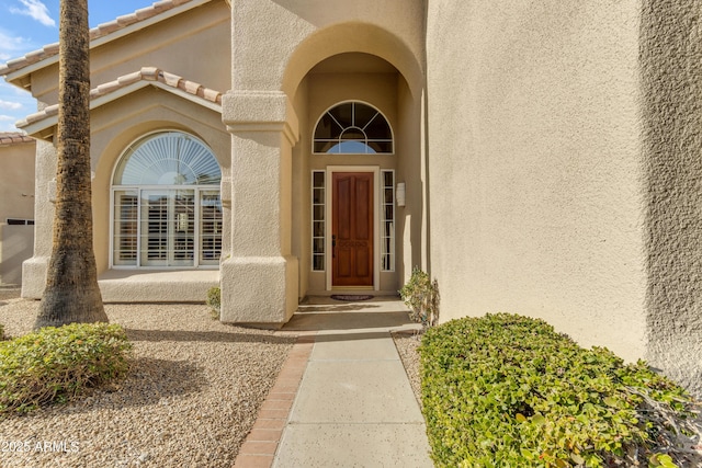 view of exterior entry with a tiled roof and stucco siding