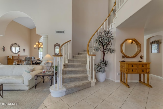 stairway with arched walkways, an inviting chandelier, a towering ceiling, and tile patterned floors