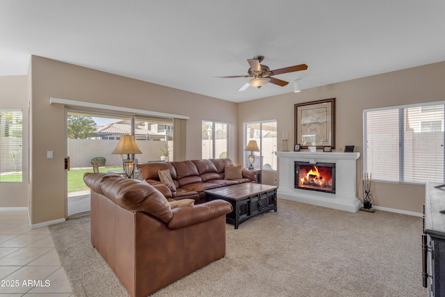 living area with a warm lit fireplace, ceiling fan, light tile patterned floors, light carpet, and baseboards