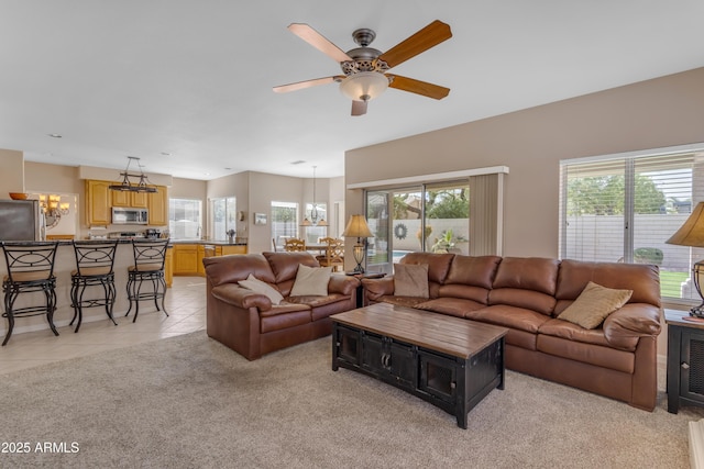 living area featuring light carpet, ceiling fan with notable chandelier, a wealth of natural light, and light tile patterned flooring