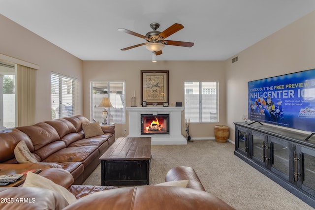 carpeted living room with a healthy amount of sunlight, visible vents, a lit fireplace, and baseboards