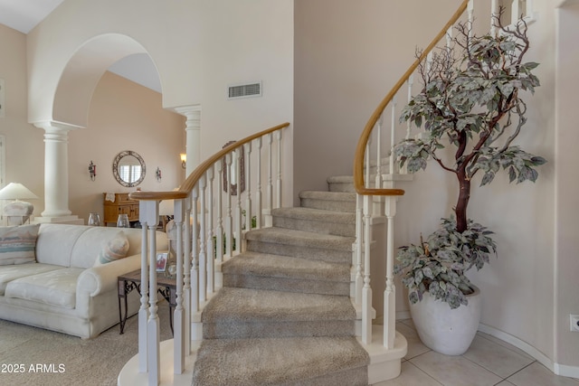 staircase with arched walkways, decorative columns, visible vents, a towering ceiling, and tile patterned flooring