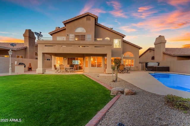 back of property at dusk with a lawn, a patio area, a balcony, and stucco siding