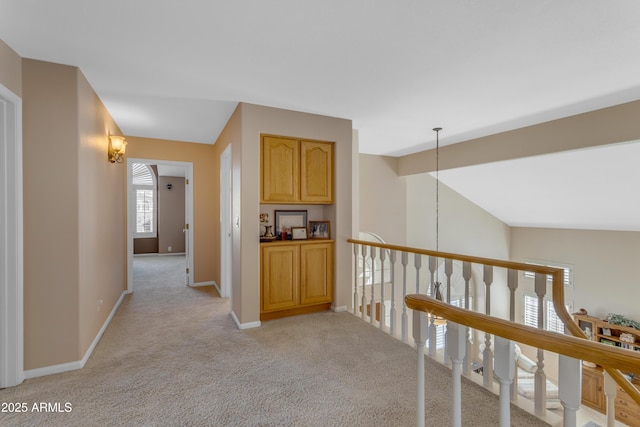 corridor with baseboards, vaulted ceiling, and light colored carpet