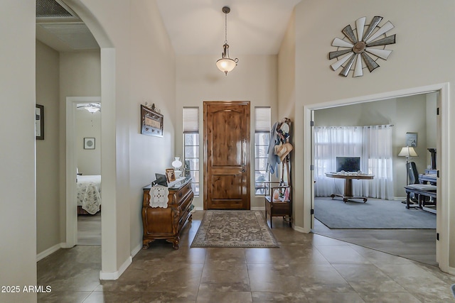 tiled entryway with arched walkways, a towering ceiling, and baseboards