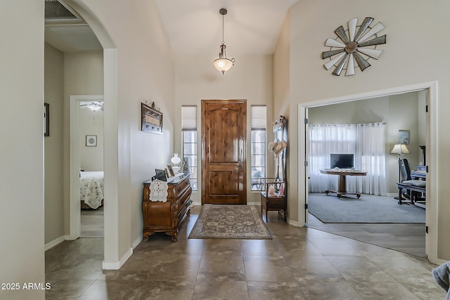 foyer featuring arched walkways, visible vents, a towering ceiling, and baseboards