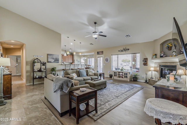 living room featuring visible vents, arched walkways, a ceiling fan, a tiled fireplace, and high vaulted ceiling