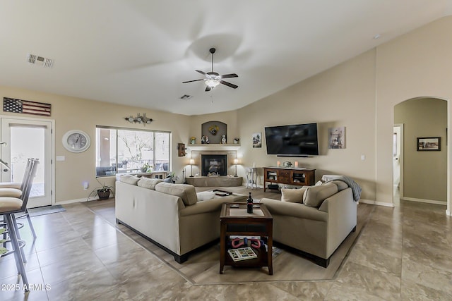 living area featuring ceiling fan, visible vents, arched walkways, and a tiled fireplace