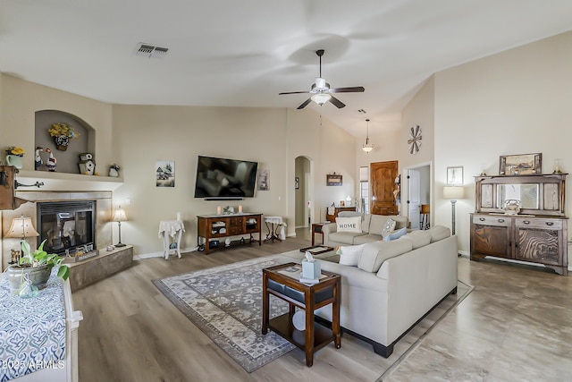 living room featuring arched walkways, visible vents, a ceiling fan, high vaulted ceiling, and a tile fireplace