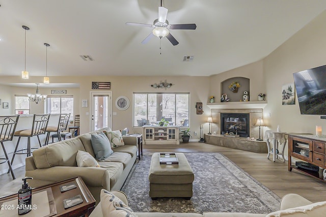 living room featuring ceiling fan with notable chandelier, a tiled fireplace, wood finished floors, and visible vents