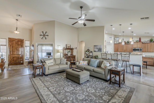 living room with arched walkways, a high ceiling, light wood finished floors, and visible vents