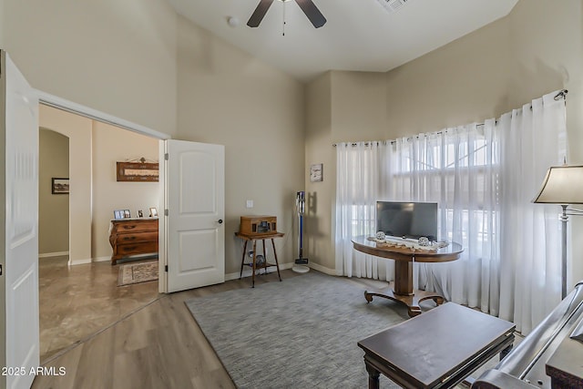 sitting room with baseboards, a high ceiling, arched walkways, and wood finished floors